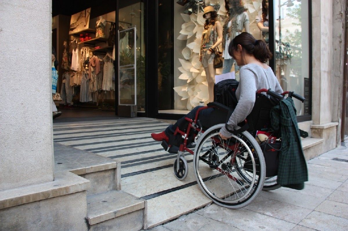 Una noia entra amb cadira de rodes en un establiment