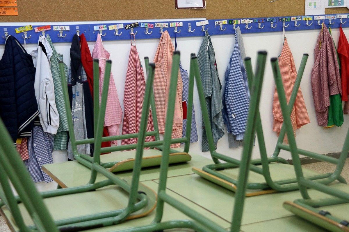Una renglera de bates penjades al penjador d'una escola, amb totes les cadires de l'aula cap per avall en primer pla.